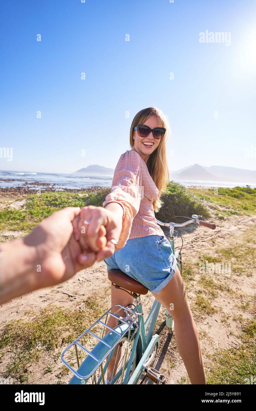 POV donna felice in bicicletta che tiene la mano sul soleggiato sentiero della spiaggia Foto Stock