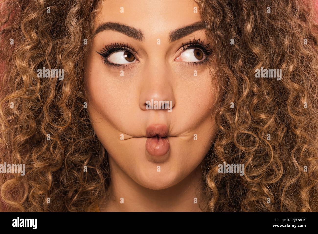 Primo piano ritratto di giovane donna guardando via con divertente espressione premendo le labbra mentre si è in piedi in studio Foto Stock