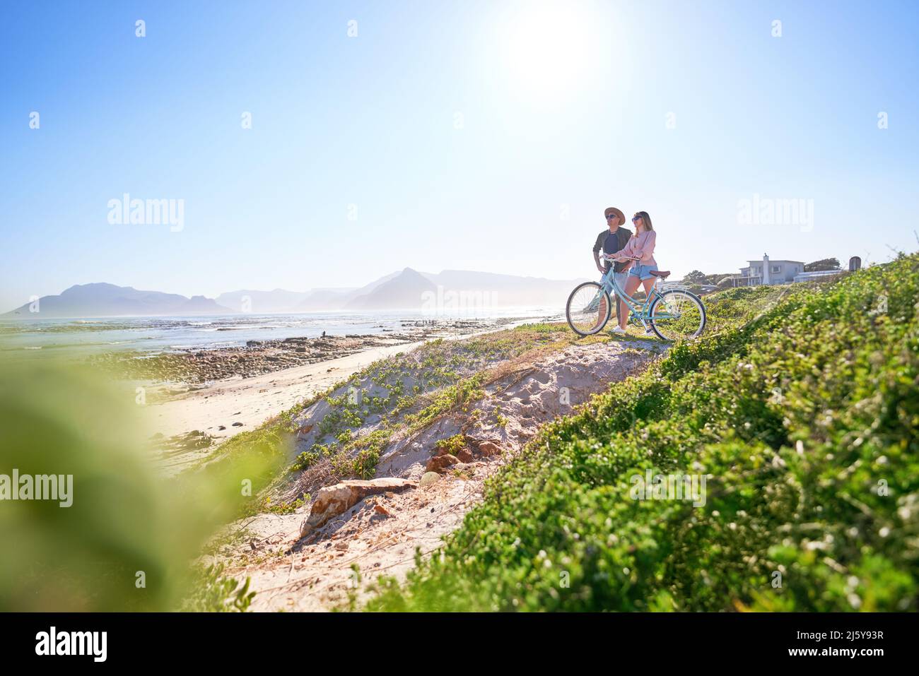 Coppia con la bicicletta sul soleggiato, spiaggia sabbiosa Foto Stock