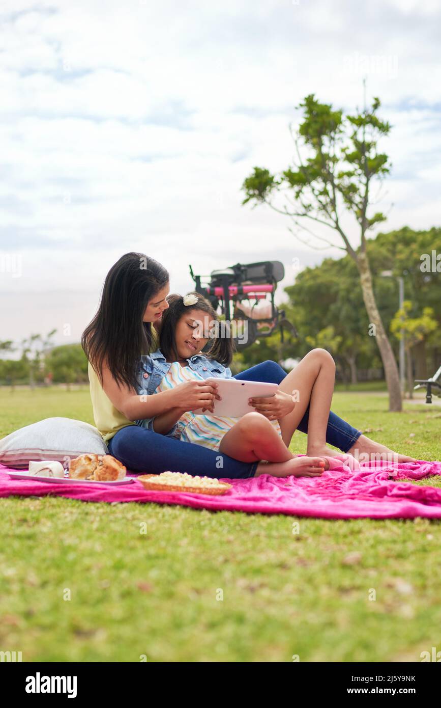 Madre e figlia disabile che usano il tablet digitale in coperta nel parco Foto Stock