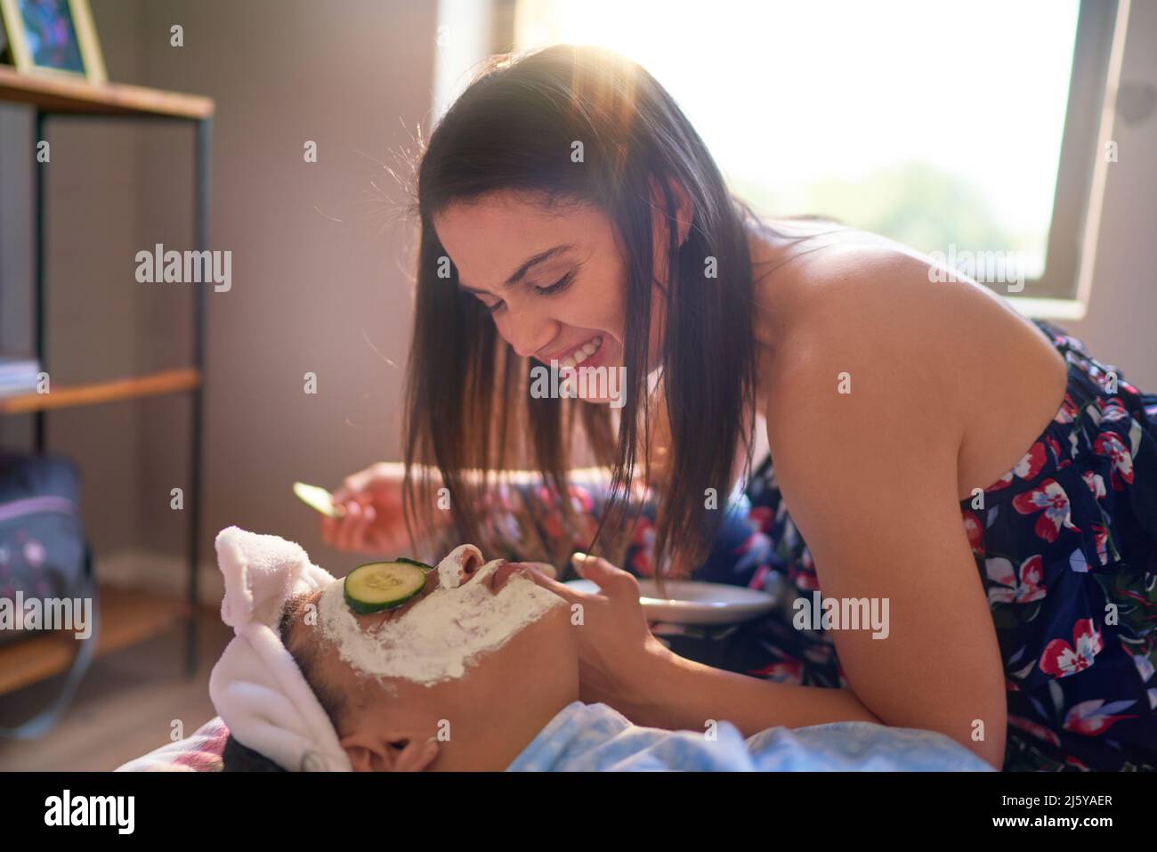 Felice madre che dà alla figlia un cetriolo viso a casa Foto Stock