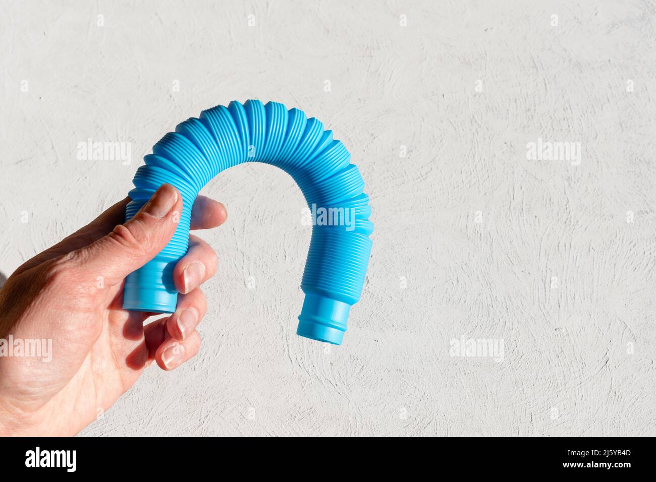 Mano femminile che tiene un tubo pop sensoriale anti-stress su sfondo bianco. Affrontare lo stress negli adulti. Relax per adulti. tubo corrugato flessibile pi Foto Stock
