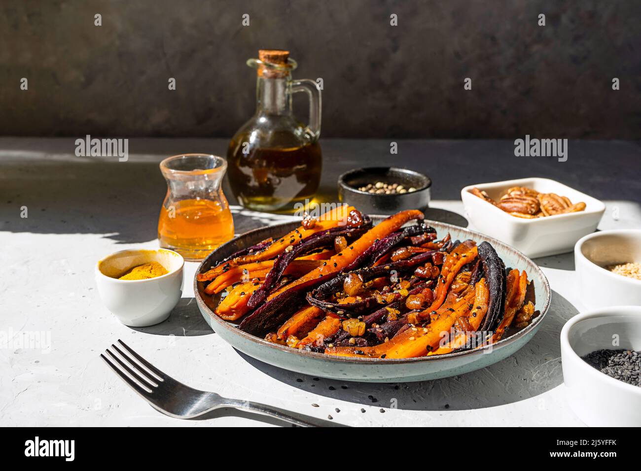 Carote di viola piccante e arancio glassate con ingredienti su sfondo grigio. Primo piano Foto Stock