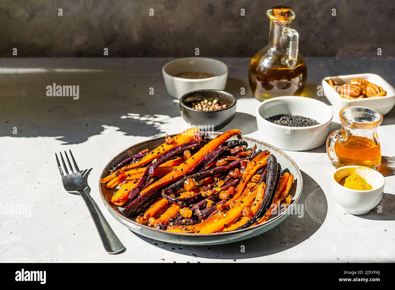Carote di viola piccante e arancio glassate con ingredienti su sfondo grigio. Primo piano Foto Stock
