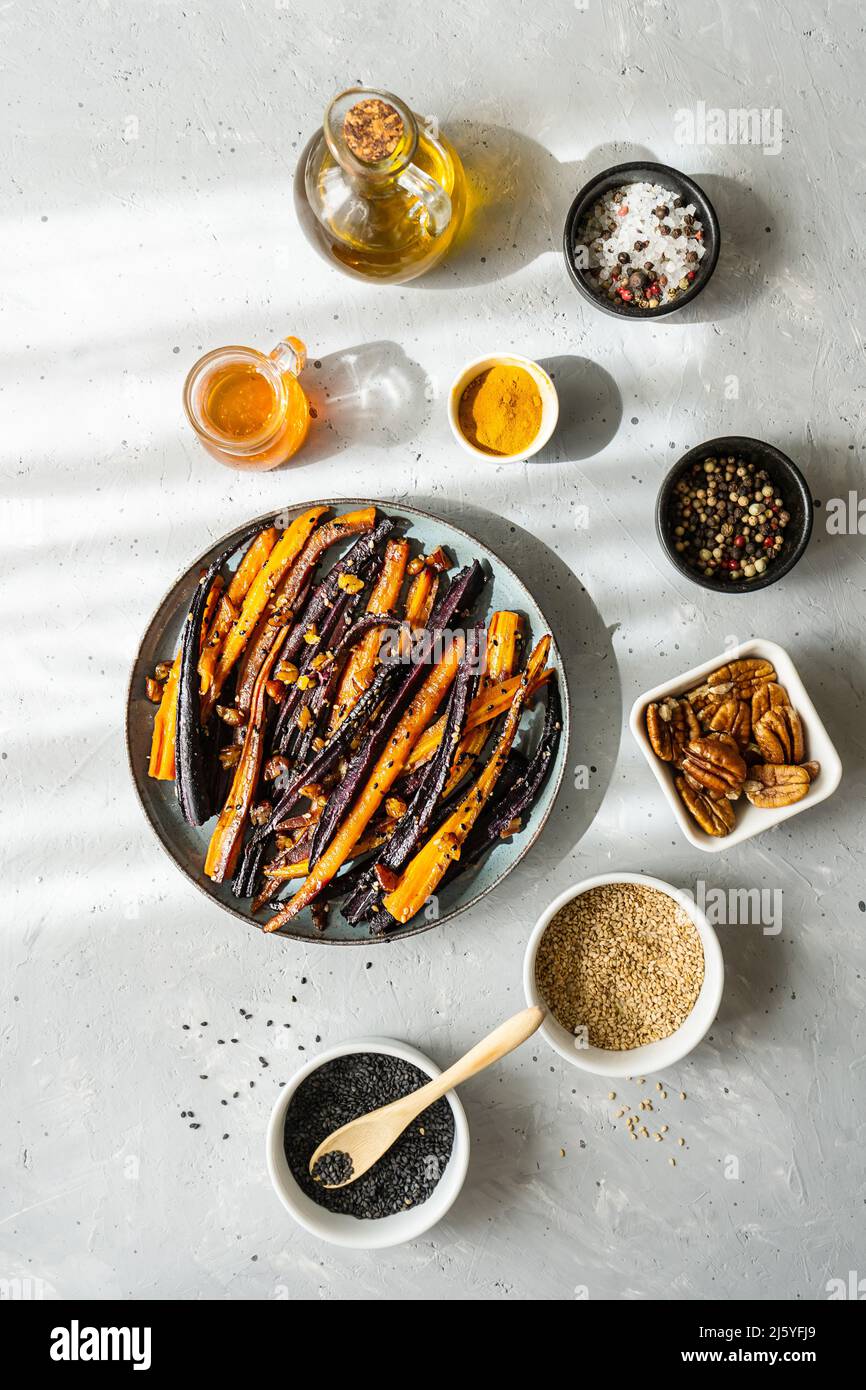 Carote viola piccanti e arancioni glassate al forno con ingredienti su sfondo grigio. Vista dall'alto Foto Stock
