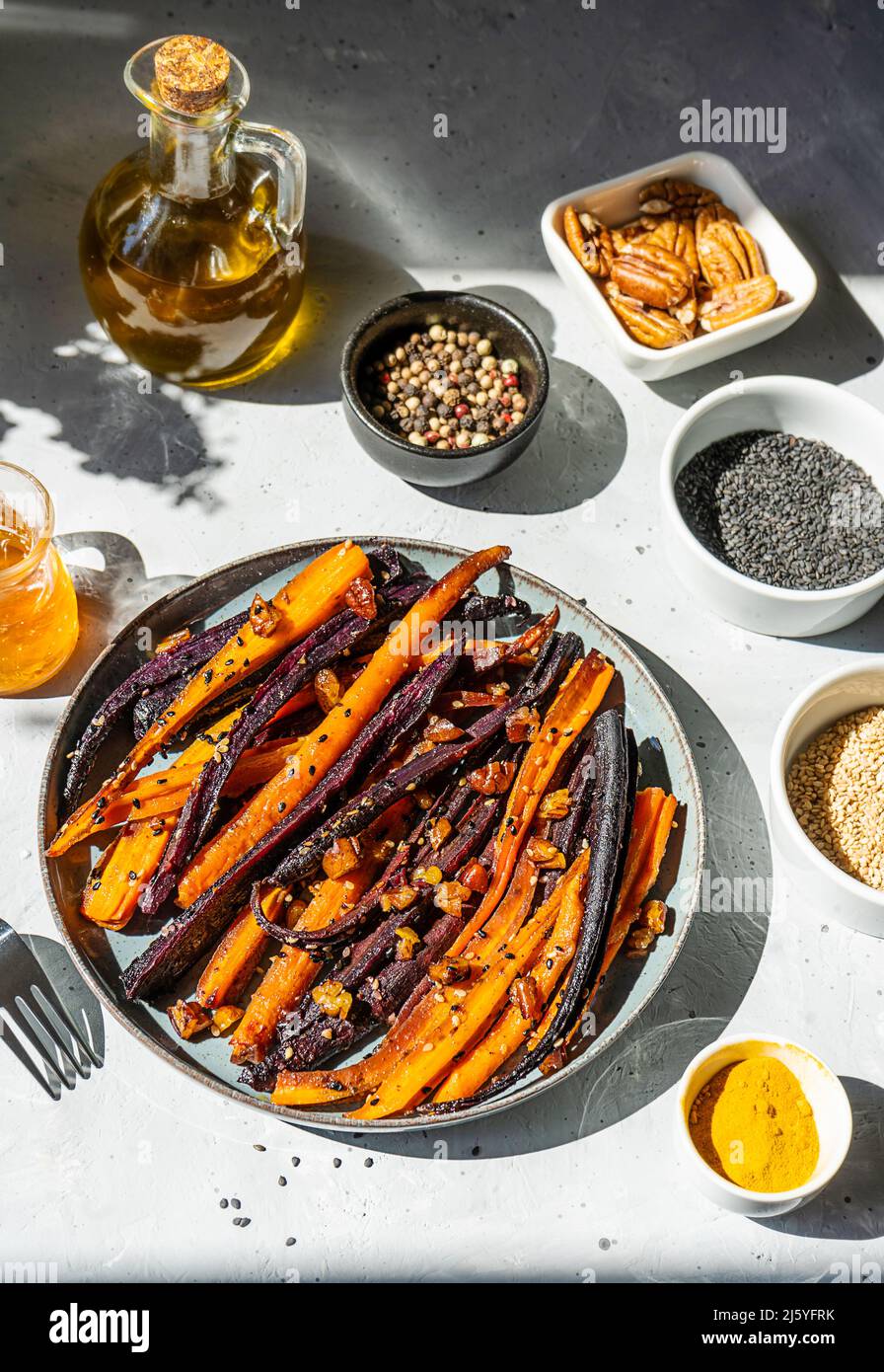 Carote viola piccanti e arancioni glassate al forno con ingredienti su sfondo grigio. Vista dall'alto Foto Stock