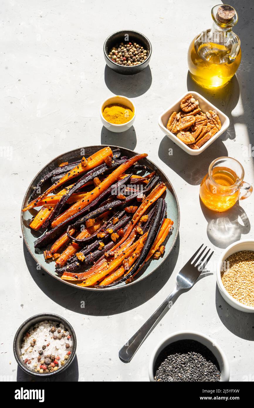 Carote viola piccanti e arancioni glassate al forno con ingredienti su sfondo grigio. Vista dall'alto Foto Stock