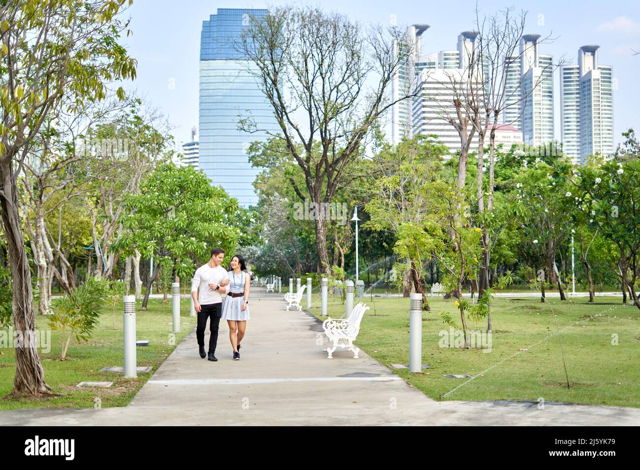 Coppia camminando attraverso un parco urbano con grattacieli sullo sfondo Foto Stock