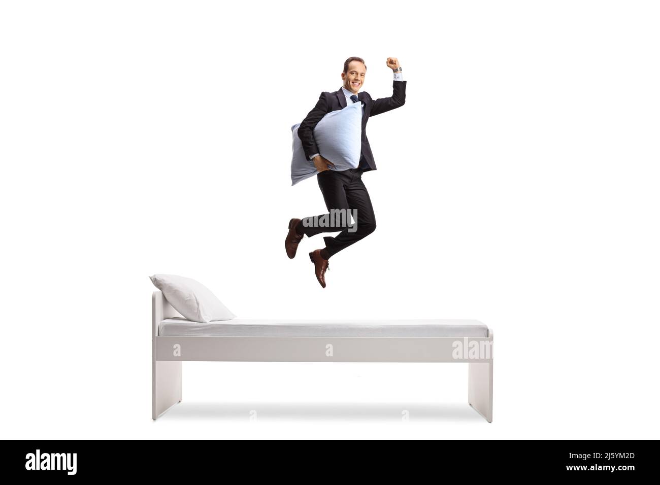 Full length shot di un uomo d'affari felice che tiene un cuscino e saltare sopra il letto isolato su sfondo bianco Foto Stock