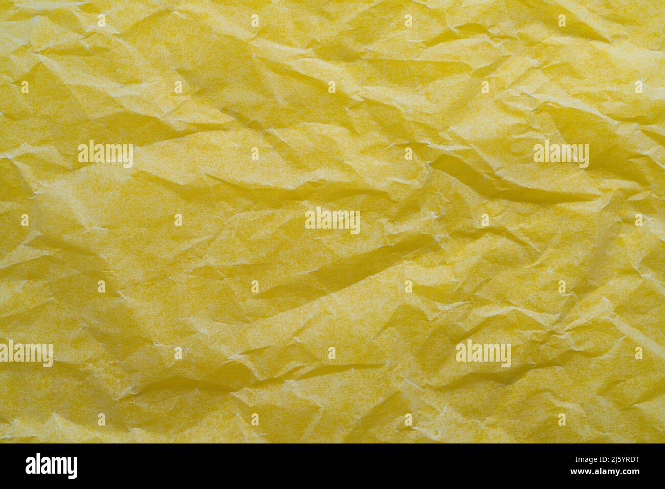 i riflessi di luce su un foglio di carta sbriciolato su una superficie gialla Foto Stock