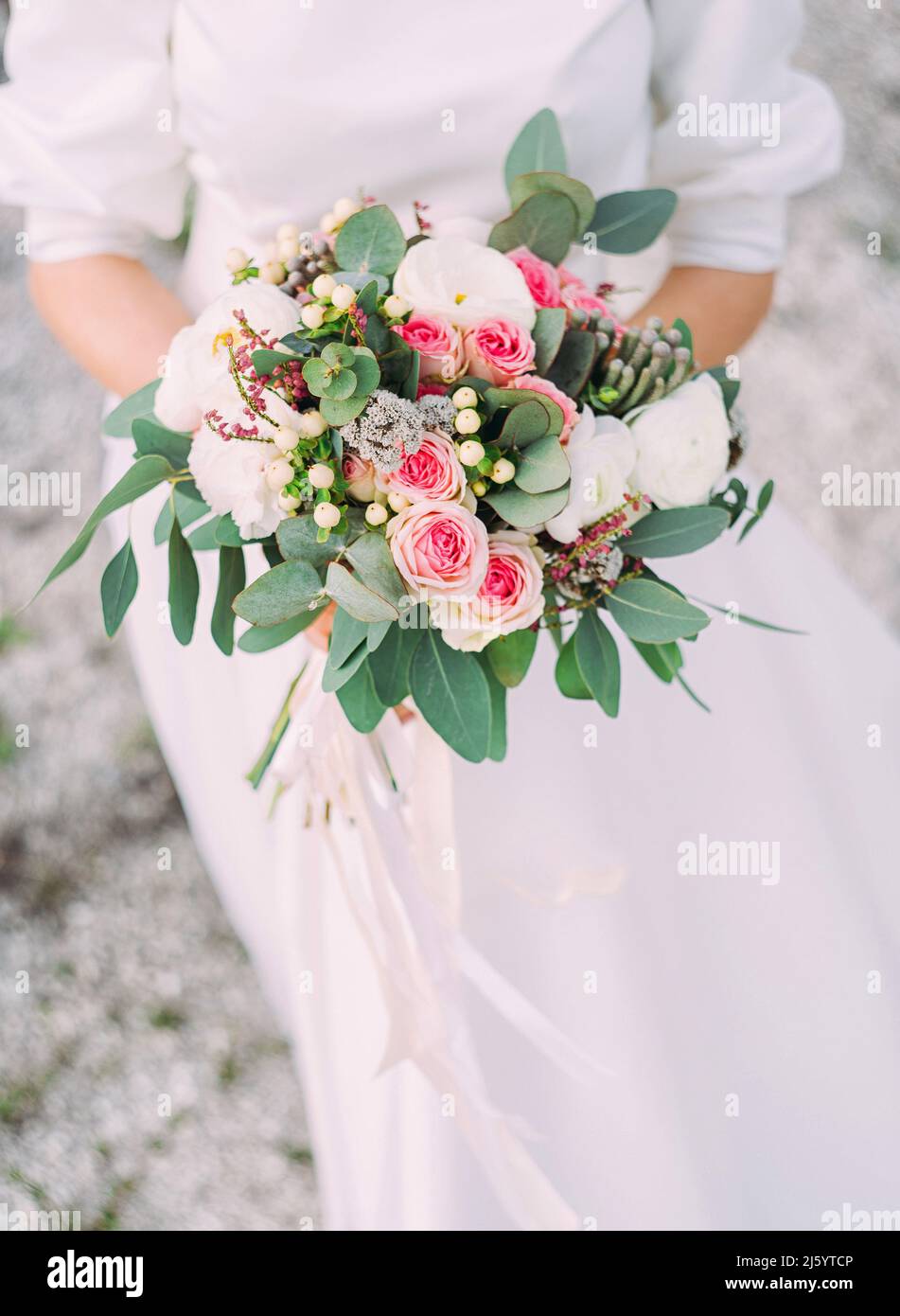 Bouquet da sposa in primo piano nei colori bianco, avorio, rosa e verde. Spiaggia di sabbia, cerimonia ventosa. Sposa in classico abito in pizzo bianco tiene nella sua modalità mani Foto Stock