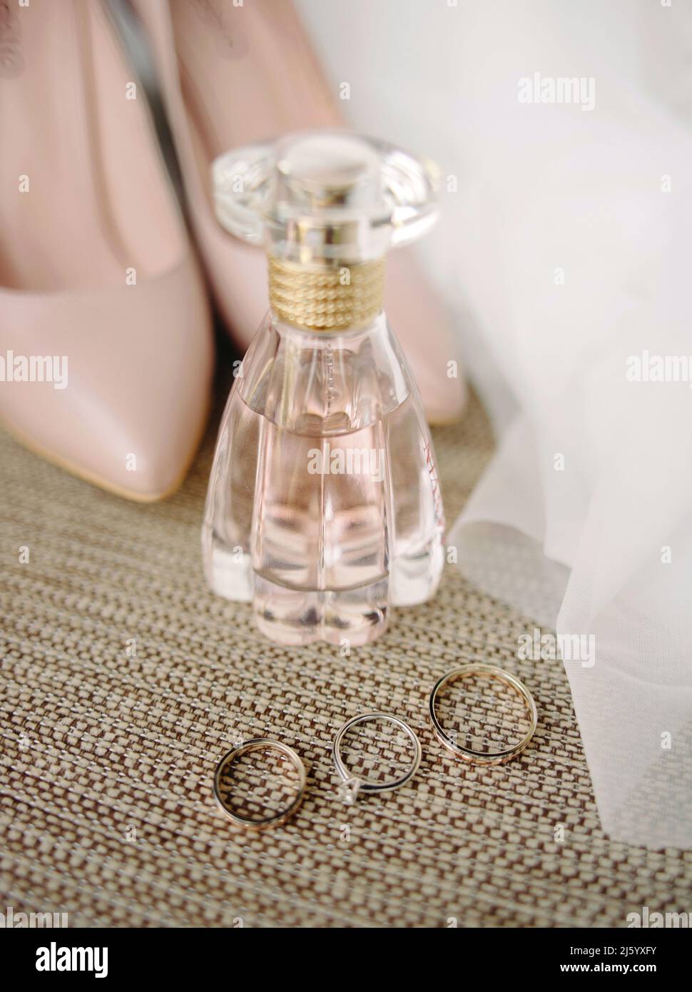 Accessori da sposa rosa. Anelli di nozze dorati e anello di aggancio con un diamante, bottiglia di profumo e polvere rosa, scarpe polverose Foto Stock