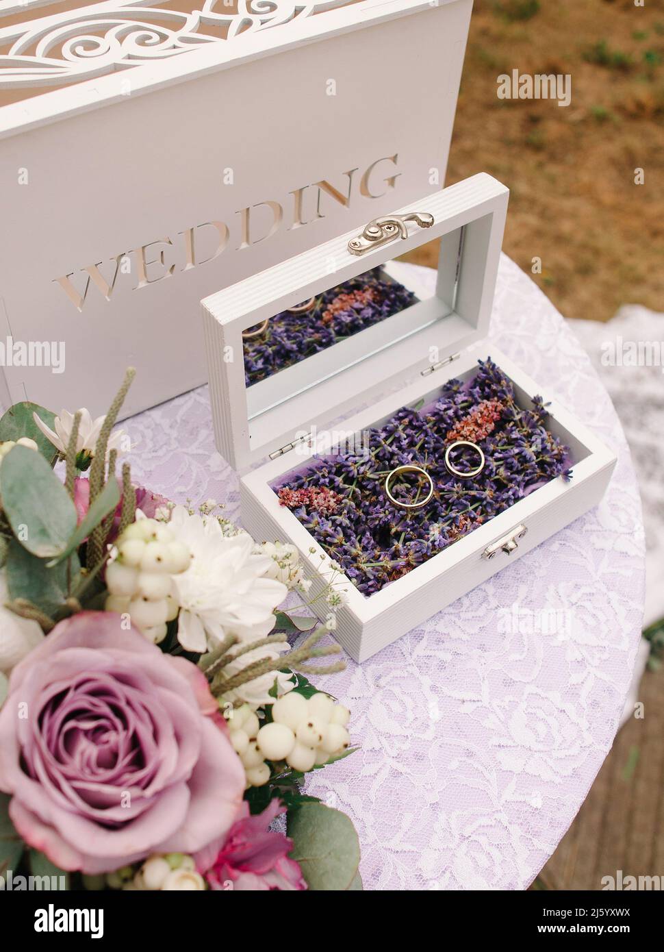 Matrimonio alla lavanda. Anelli di nozze con decorazioni floreali viola sul primo piano del tavolo bianco. Foto Stock