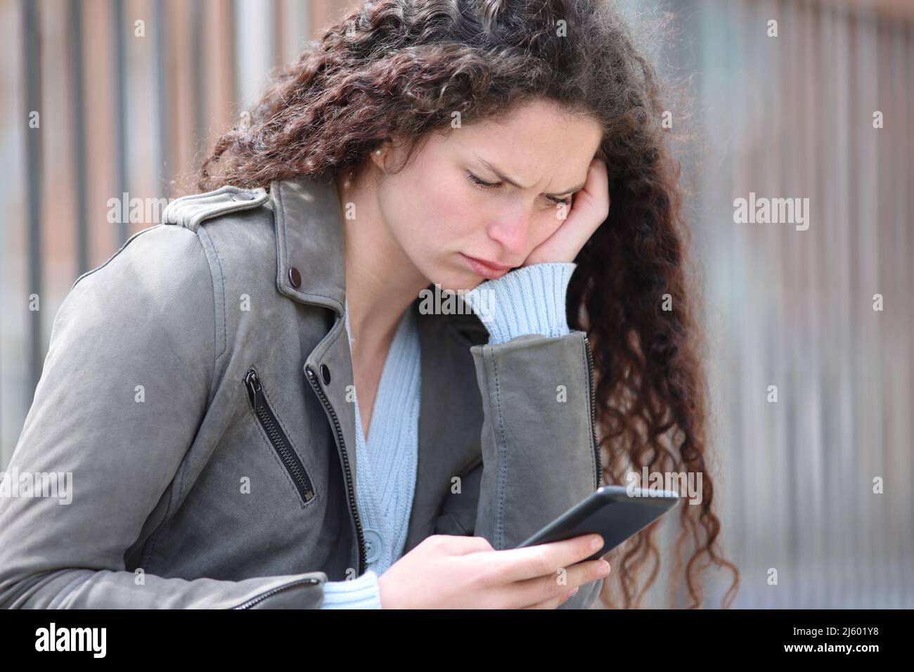 Donna confuso che controlla il contenuto dello smartphone seduto in strada Foto Stock