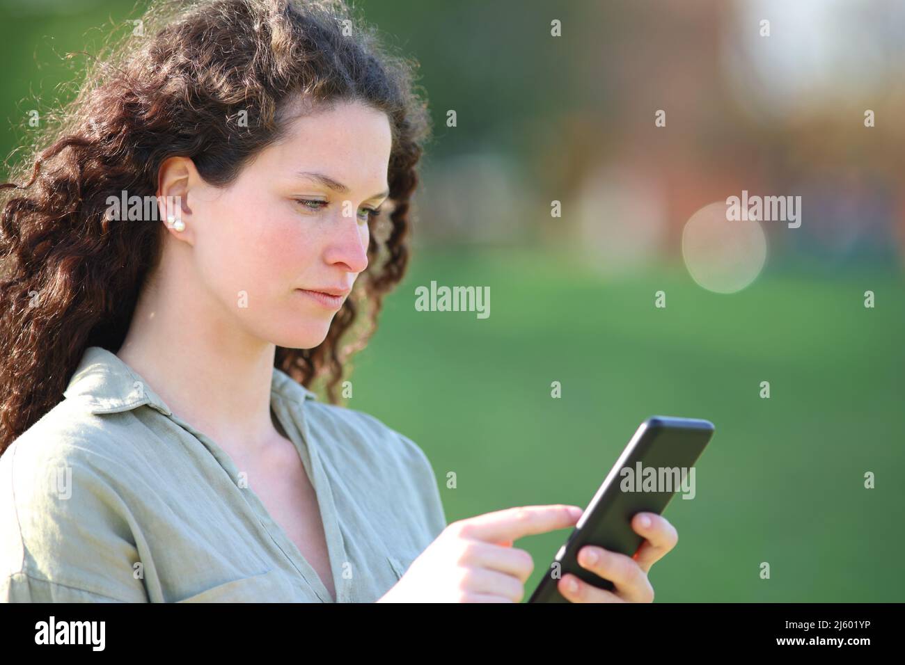 Donna seria che usa lo smart phone che cammina in un parco una giornata di sole Foto Stock