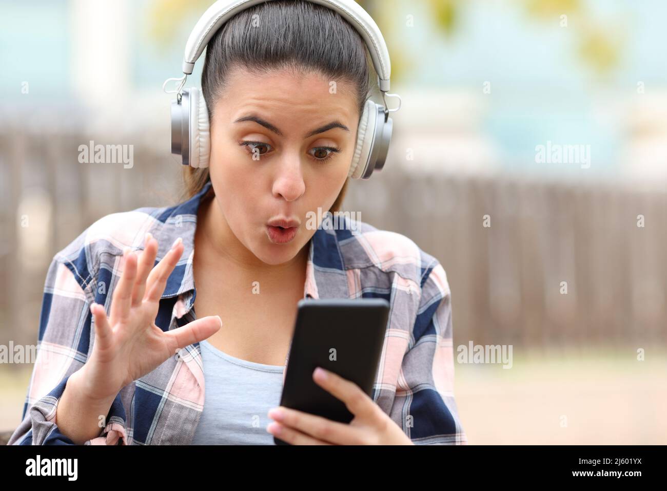 Vista frontale ritratto di un teen stupito che ascolta musica trovare contenuti del telefono in un parco Foto Stock