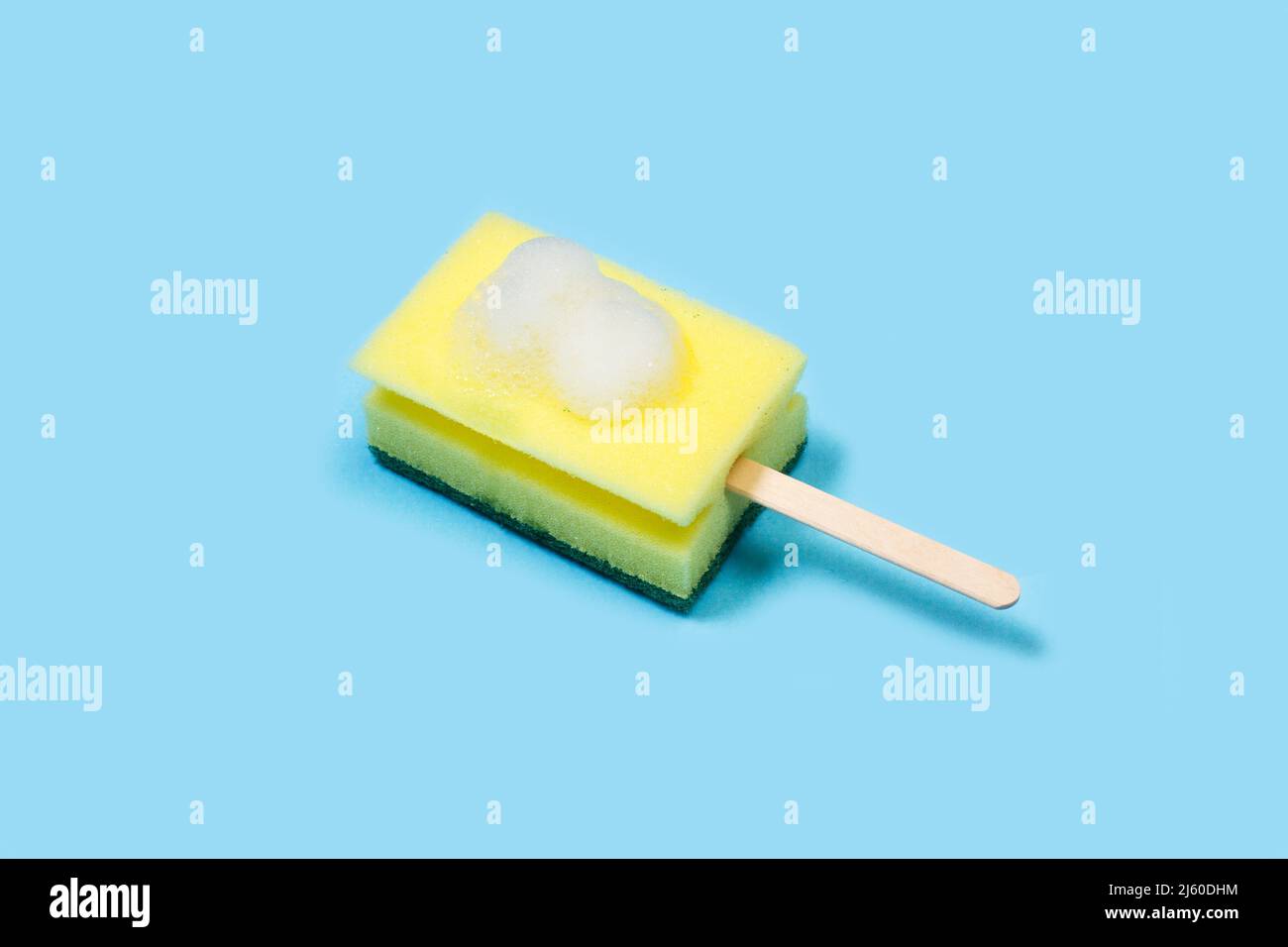 Spugna per la pulizia con un bastoncino per gelato e schiuma di sapone su sfondo blu chiaro Foto Stock