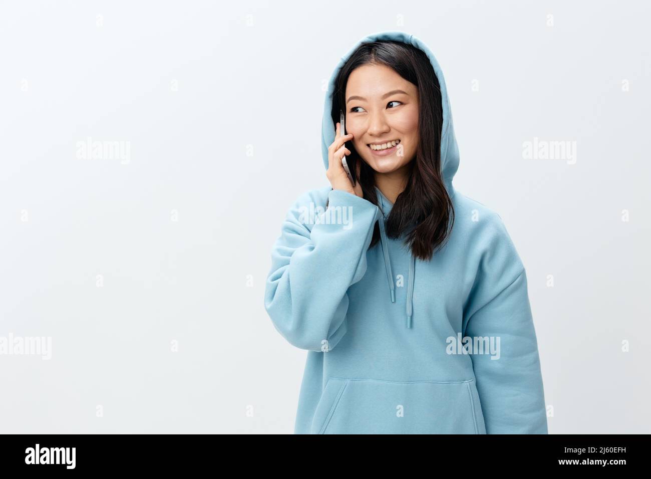 Bella felice Coreano giovane femmina in blu Hoodie tenere telefono parla con il ragazzo posa isolato su sfondo bianco studio. La migliore offerta Foto Stock