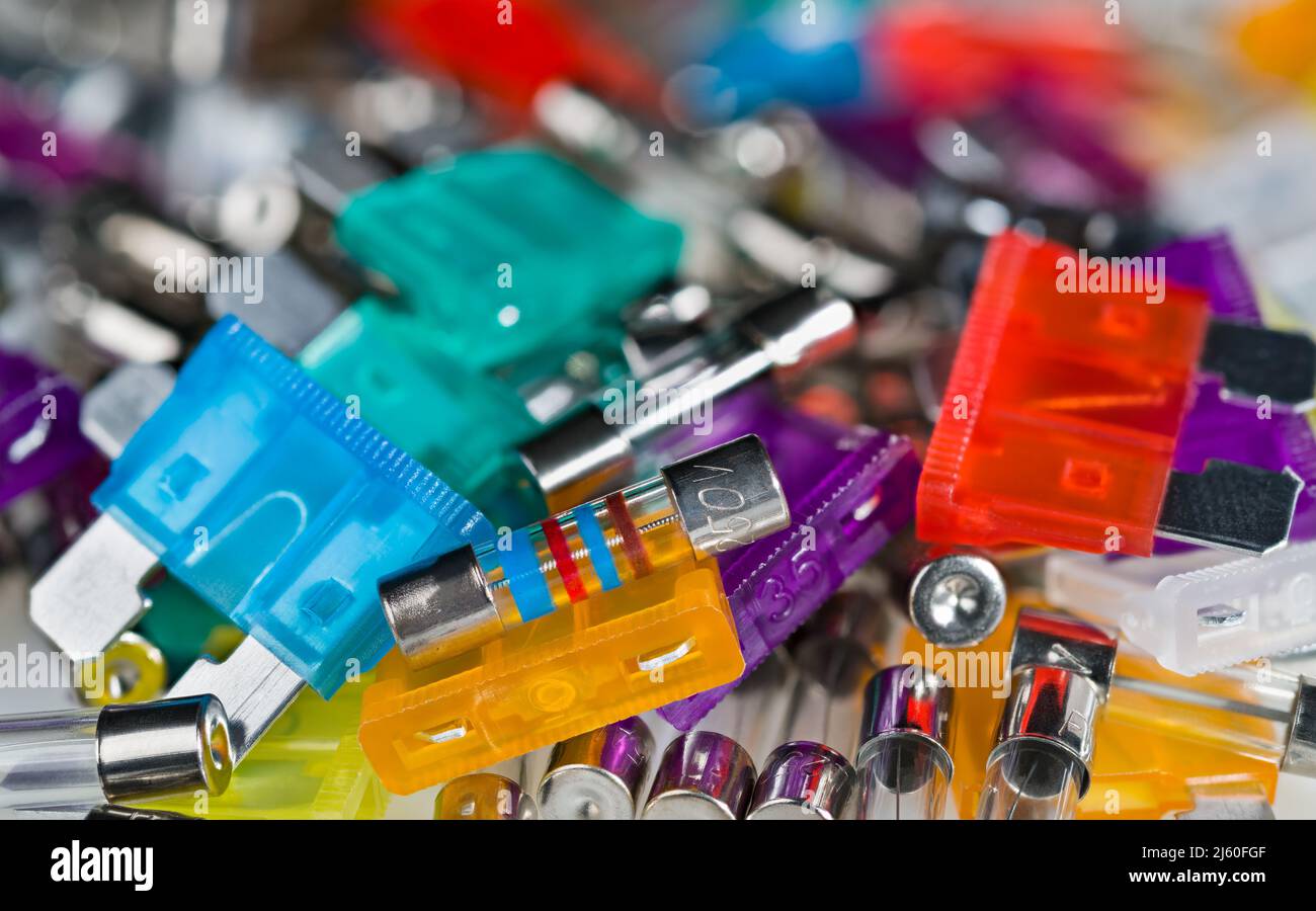 Primo piano di vari fusibili di corrente elettrica mucchio con bokeh in sfondo sfocato. Componenti elettronici di sicurezza per la protezione da sovracorrente. E-Waste heap. (Cumulo rifiuti elettronici) Foto Stock