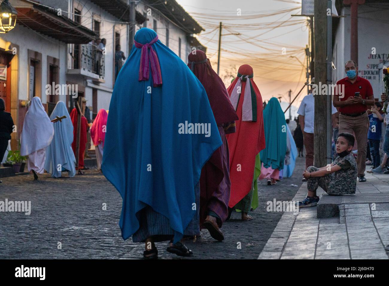 Un giovane guarda la processione del silenzio per le strade in occasione della celebrazione del Sabato Santo, 16 aprile 2022 a Patzcuaro, Michoacan, Messico. La piccola città indigena conserva tradizioni dal dominio coloniale spagnolo compresa la confraternita dei penitenti durante la settimana Santa. Foto Stock