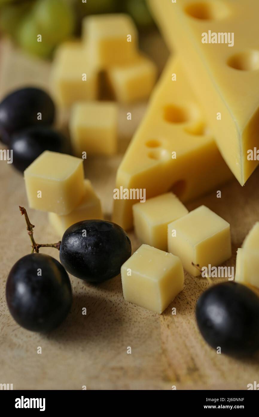 Triangoli di formaggio Mazdar, cubetti di formaggio gouda e uva nera e verde. Formaggio con uva bacche su sfondo di legno. Foto Stock