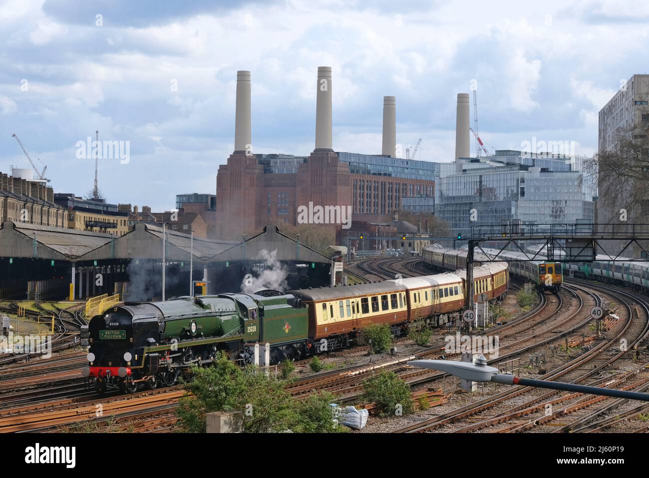 Una locomotiva a vapore Clan Line trasporta una locomotiva a vapore Belmond British Pullman a Londra Victoria con la centrale elettrica Battersea in background Foto Stock