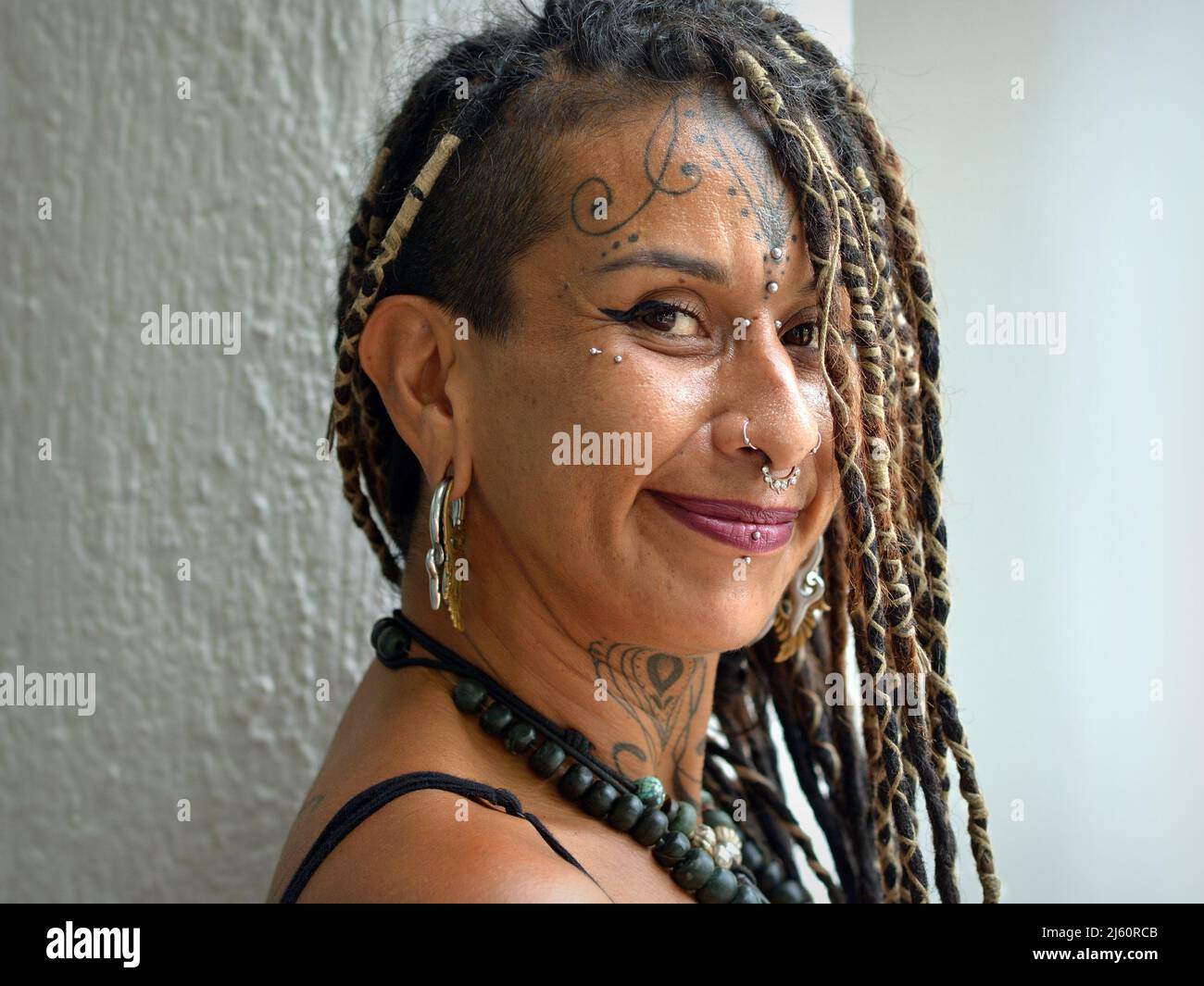 Attraente alternativa giovane messicana donna con lunghissimo temibile Rasta trecce, body art viso piercing e tatuaggio sembra positivamente ottimista al telespettatore. Foto Stock
