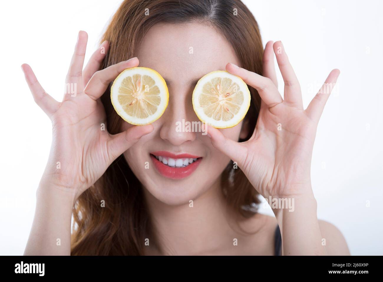 Bella giovane donna giocosamente coperto i suoi occhi con una fetta di limone, su sfondo bianco - foto di scorta Foto Stock