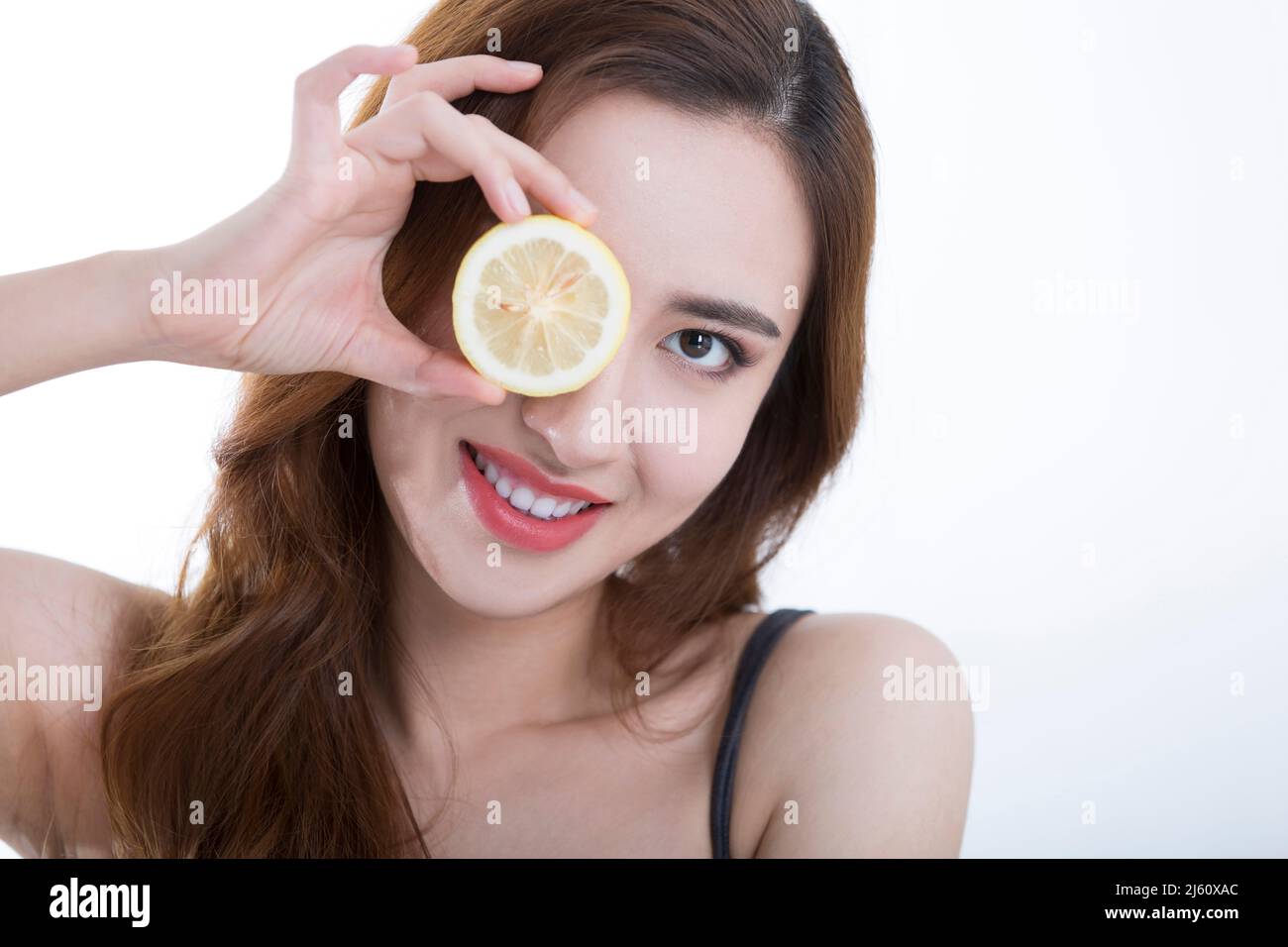 Bella giovane donna giocosamente coperto i suoi occhi con una fetta di limone, su sfondo bianco - foto di scorta Foto Stock