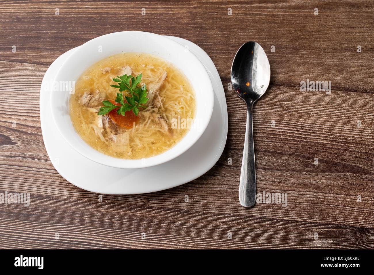 Gustoso bouillon di zuppa di pollo con spaghetti, carne di pollo, aneto e prezzemolo in un recipiente bianco. Isolato su sfondo di legno. Menu pasto sano Foto Stock