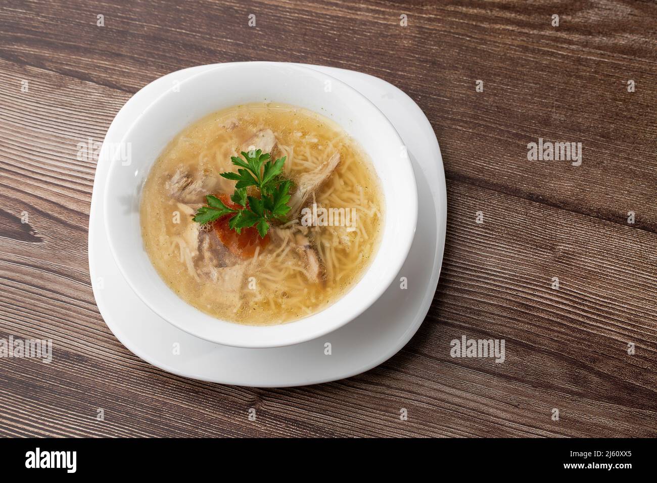 Gustoso bouillon di zuppa di pollo con spaghetti, carne di pollo, aneto e prezzemolo in un recipiente bianco. Isolato su sfondo di legno. Menu pasto sano Foto Stock