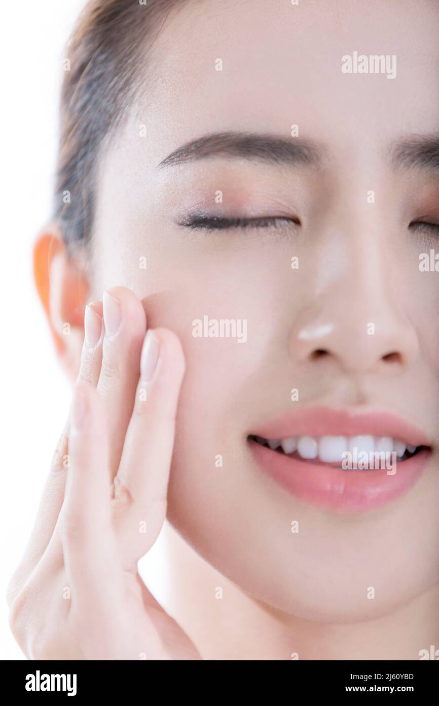 Giovane donna che aveva appena applicato prodotti per la cura della pelle stroked la sua pelle liscia con gli occhi chiusi, su sfondo bianco - foto di scorta Foto Stock