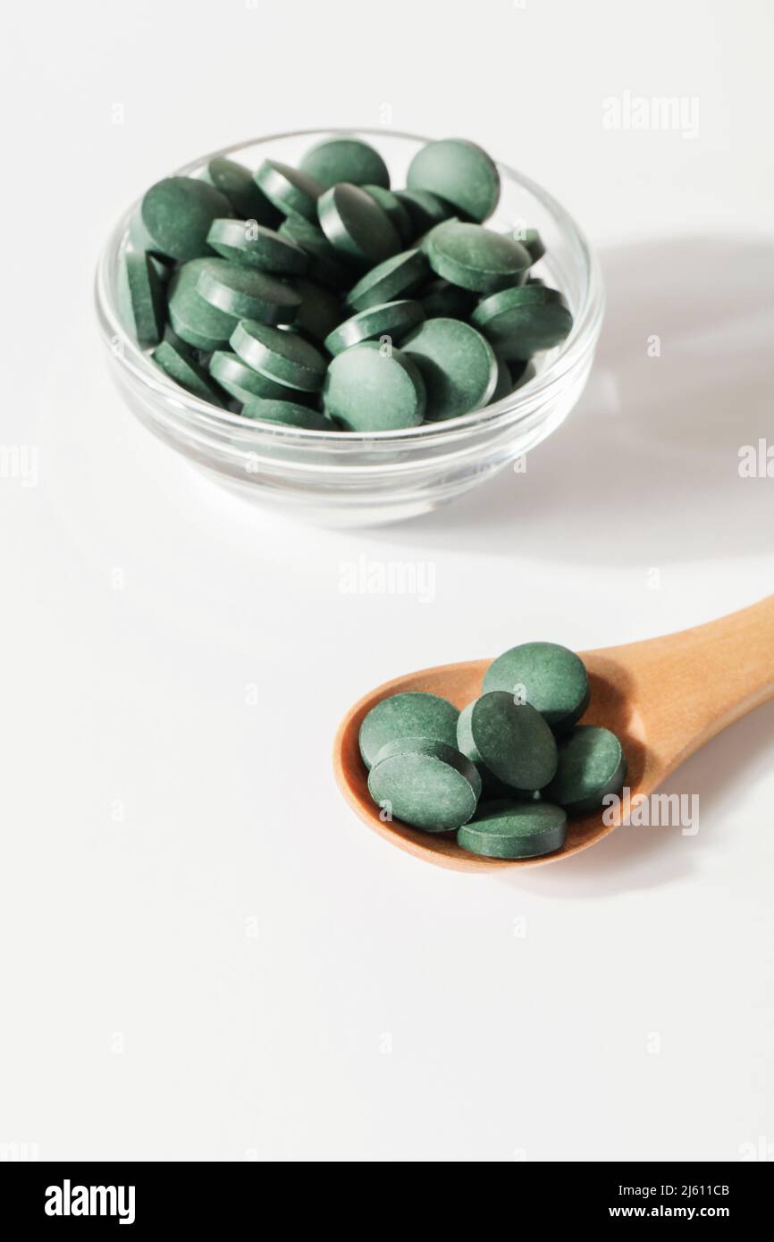 additivi naturali e superfood. pillole di alghe spirulina verde in cucchiaio e ciotola di vetro su sfondo bianco. spazio sano concept.organic copie di cibo Foto Stock