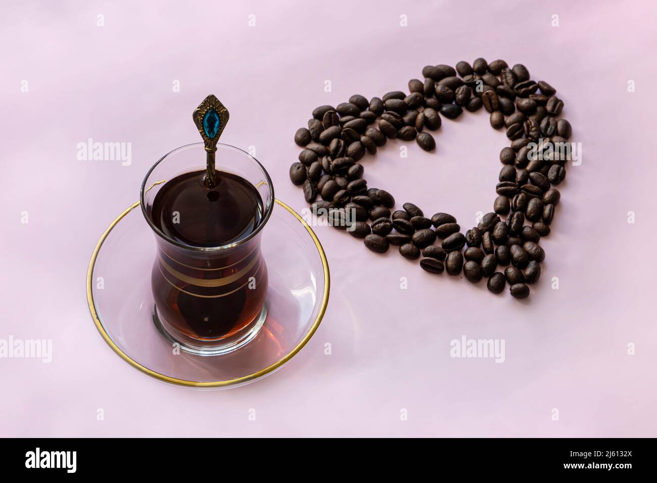 Tazza di caffè in vetro e chicchi di caffè torrefatti su sfondo rosa. Caffè mania, amore del caffè, concetto Foto Stock