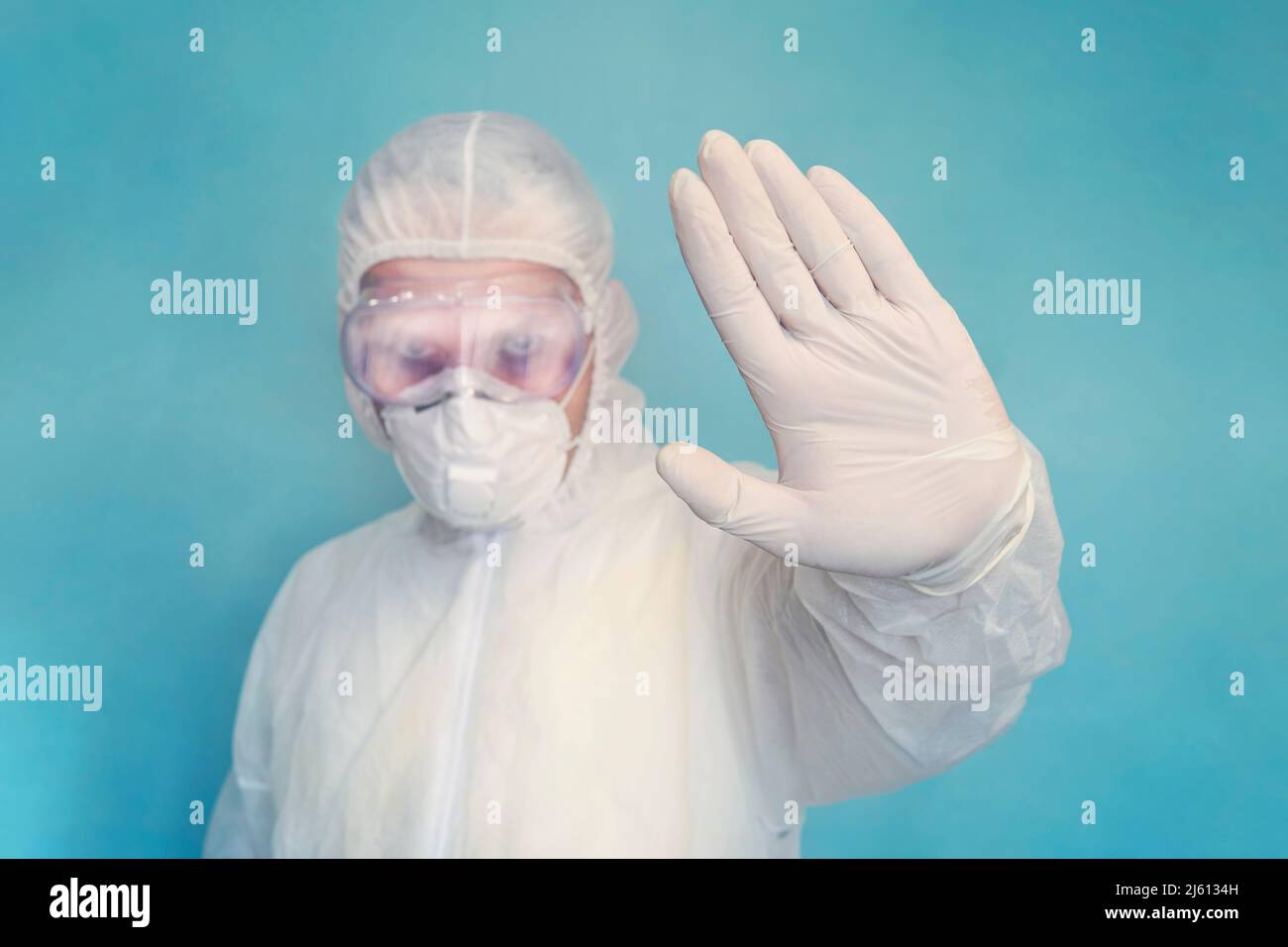 Medico con tuta completa e maschera che mostra stop segno con la sua mano su sfondo blu. Corona virus o covid-19 epidemia globale. Interrompere l'infezione Foto Stock