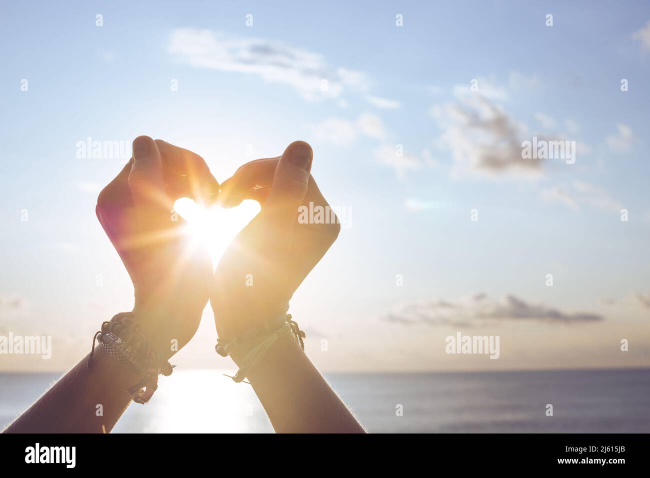 Forma del cuore che fa delle mani contro il cielo blu e il sole Foto Stock