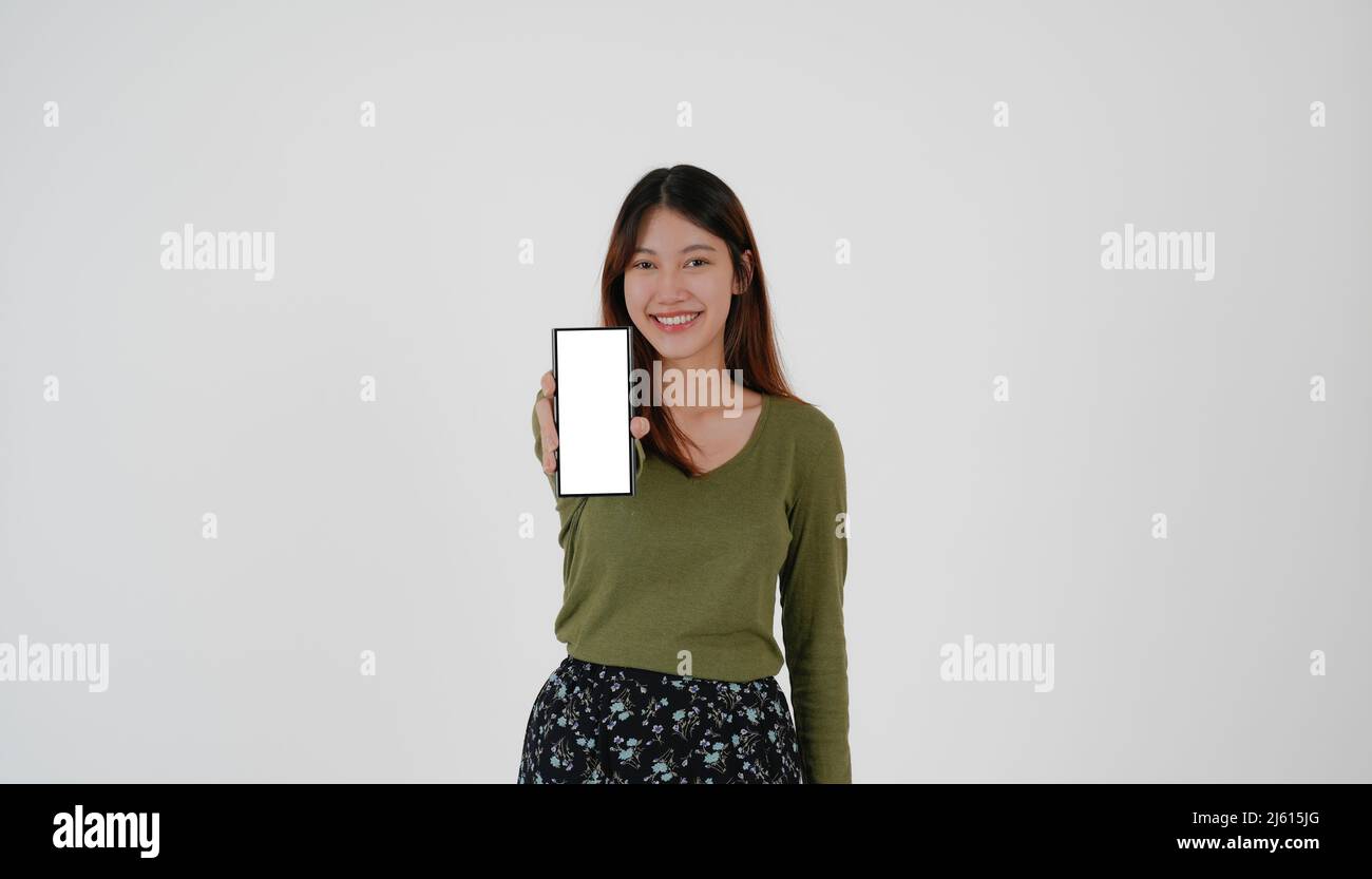 L'immagine della giovane ragazza asiatica che tiene lo smartphone mostra uno schermo bianco vuoto su sfondo bianco. Foto Stock