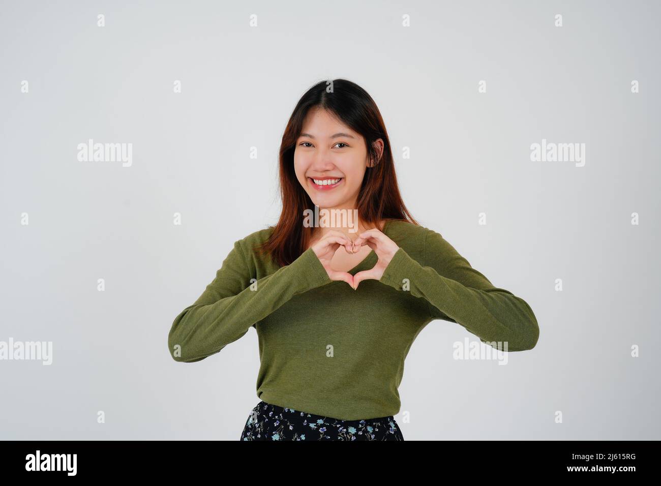 Attraente giovane donna asiatica si sente felice e forme romantiche cuore gesto esprime sentimenti teneri indossa casual jumper pose contro bianco Foto Stock