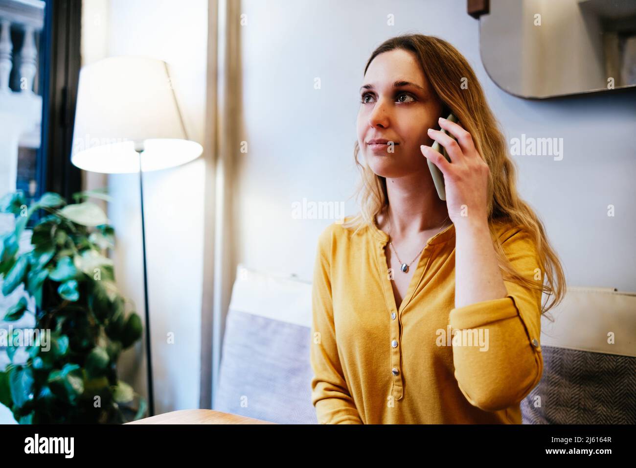giovane donna bionda attraente con camicia gialla che parla al telefono in una caffetteria Foto Stock