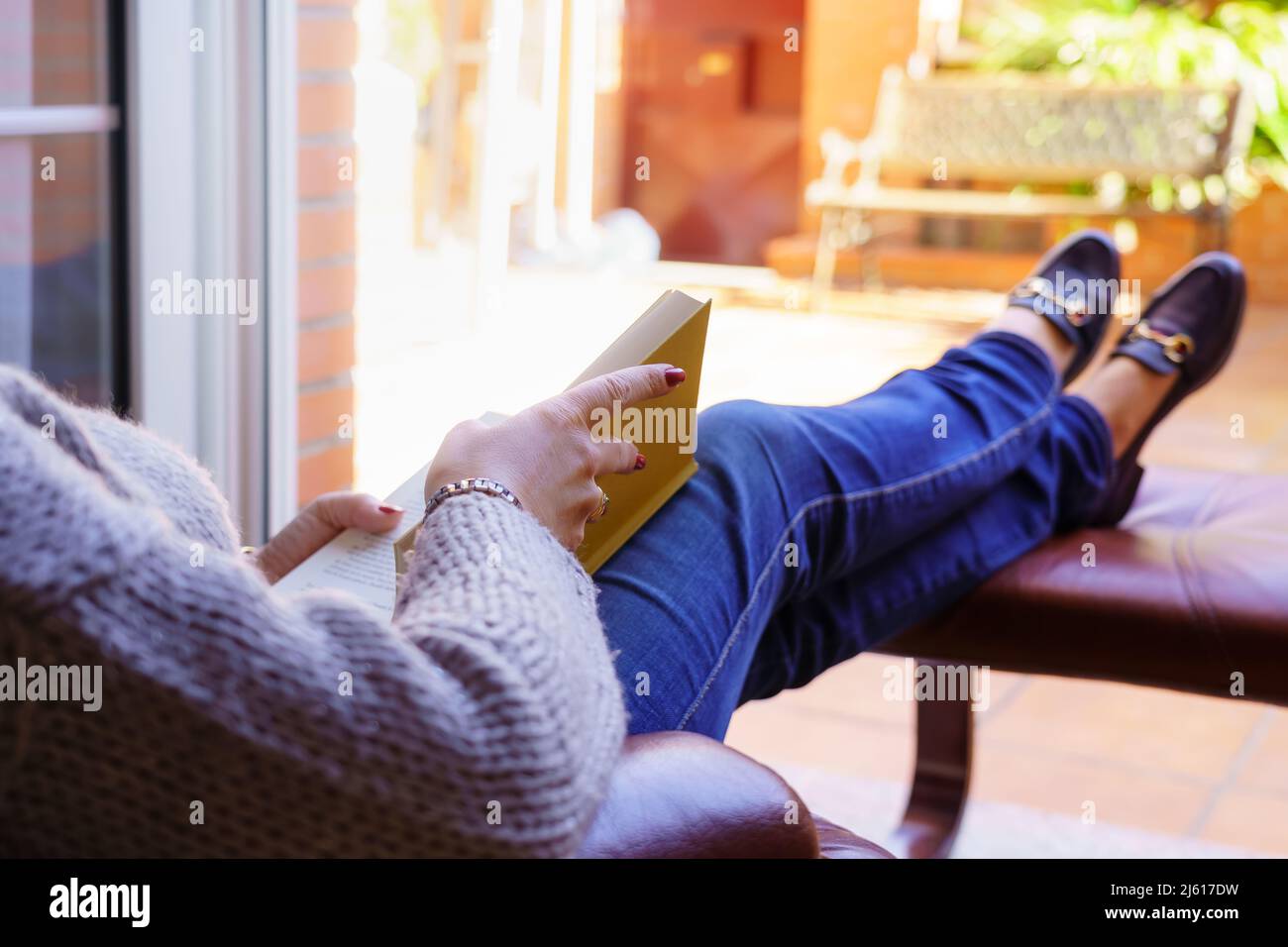 Donna bianca che legge un libro in una poltrona rilassandosi in bella luce esterna. Spazio di copia. Lettura, concetto di insegnamento. Sfondo. Foto Stock