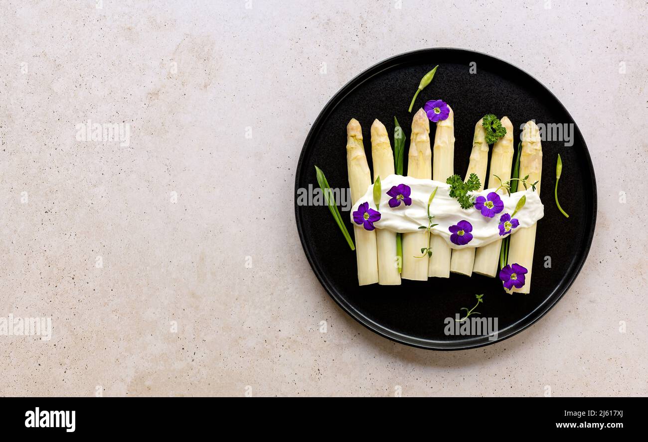 Asparagi bianchi tedeschi con salsa, aglio selvatico e fiori commestibili. Foto Stock