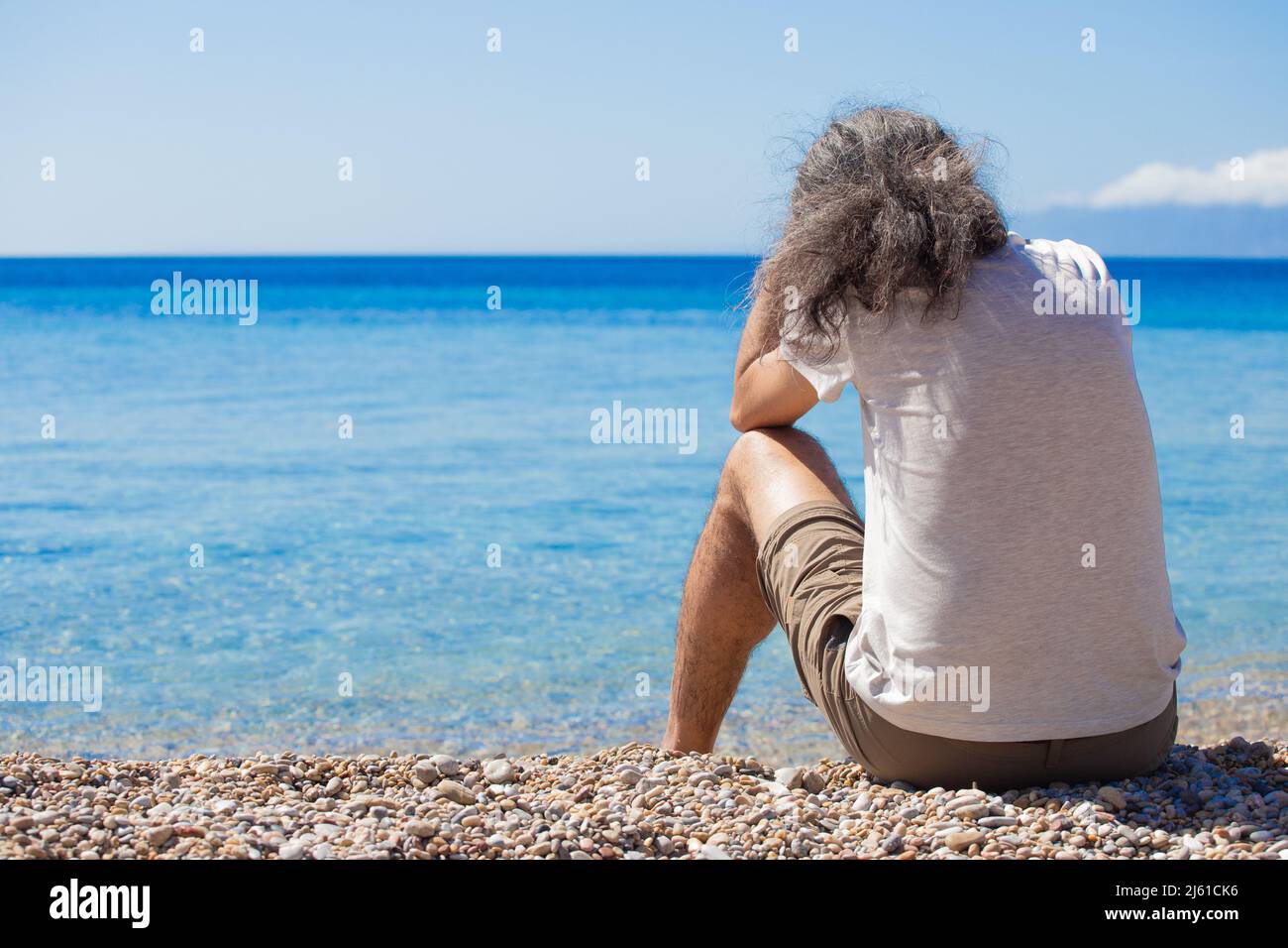 L'uomo è seduto solo dal dorso e guarda al mare blu del Mediterraneo. Orizzontale. Foto Stock