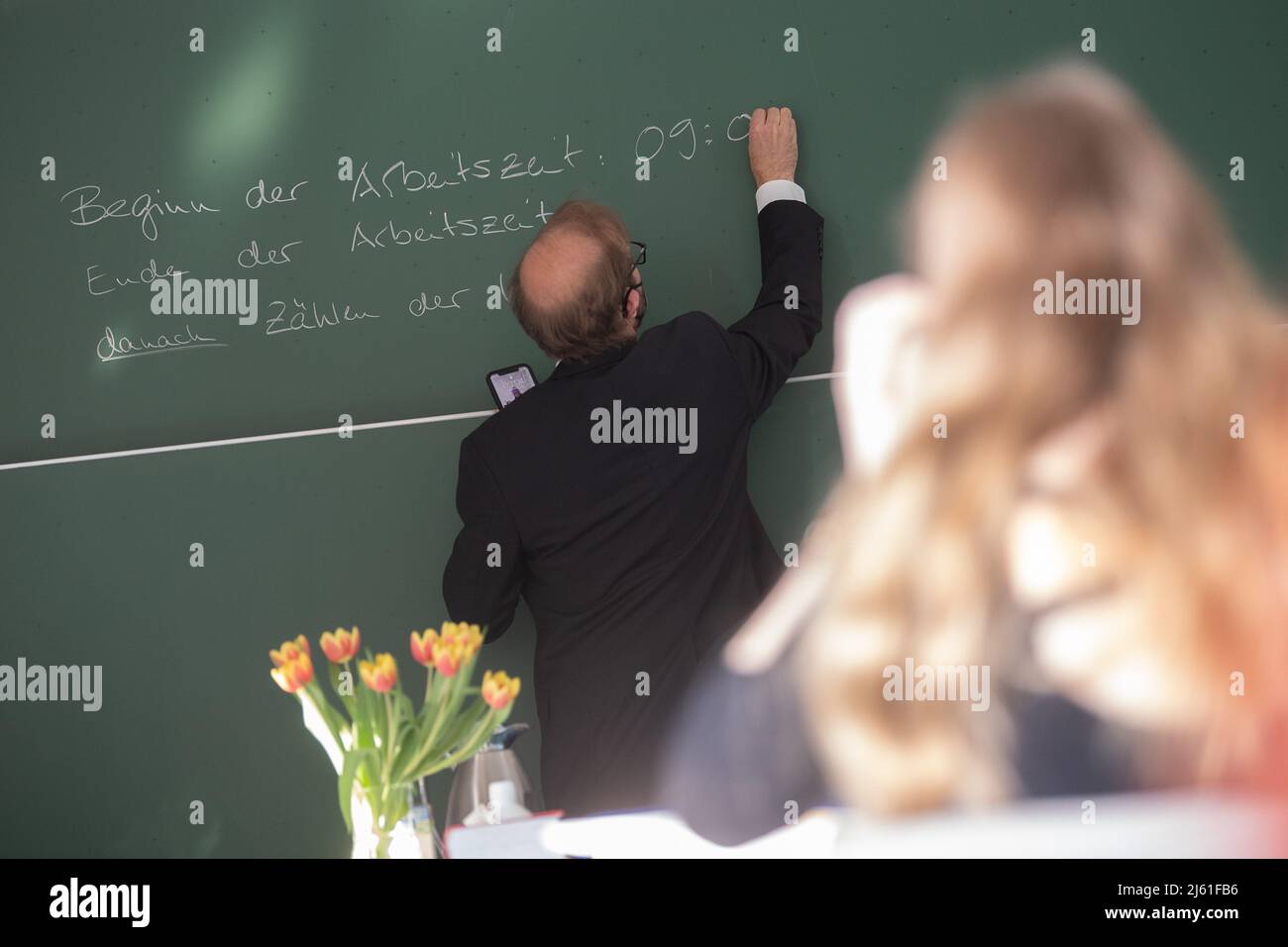27 aprile 2022, Hessen, Wölfersheim: Un insegnante scrive l'ora di inizio del corso tedesco di Abitur sulla lavagna a Singbergschule il primo giorno dei 2022 esami scritti di Abitur in Assia. Iniziano con il soggetto tedesco e terminano il 11 maggio con la chimica. Foto: Sebastian Gollnow/dpa Foto Stock
