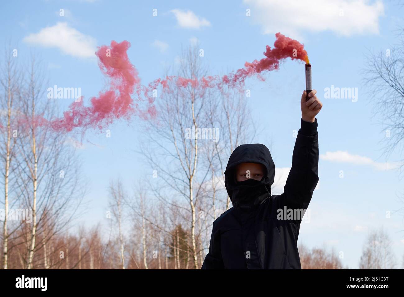 Un preteen in una giacca nera e una maschera tiene una scacchiera con fumo colorato Foto Stock