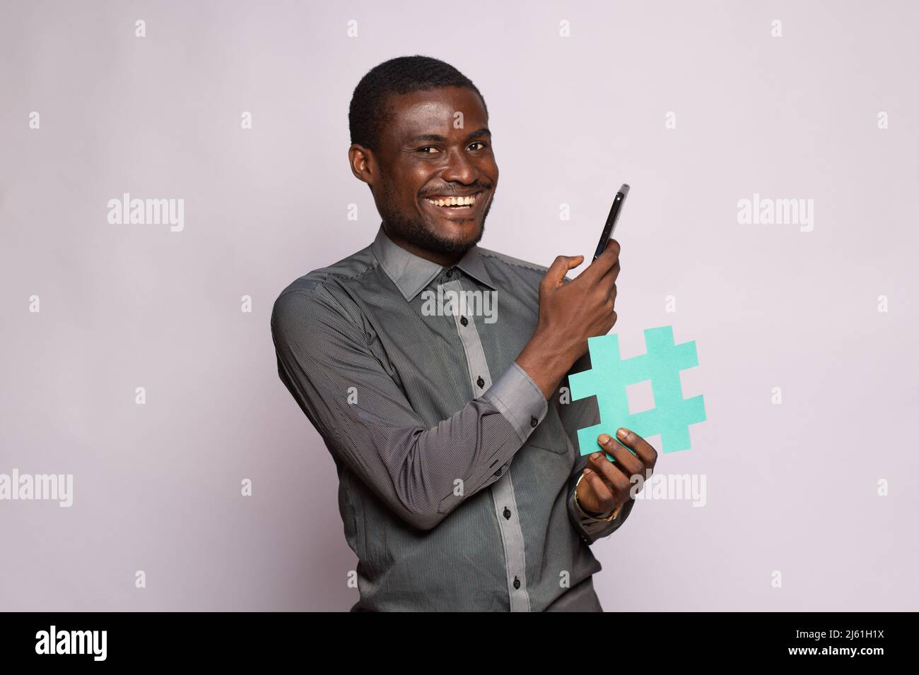 uomo nero eccitato che tiene il telefono e il simbolo dell'etichetta di hash Foto Stock