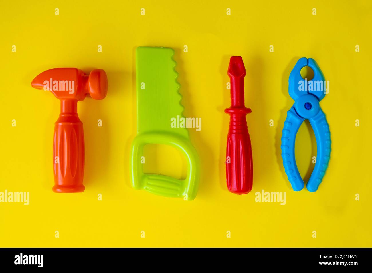 Giochi di riparazione colorati su sfondo giallo, gioco del bambino isolato su sfondo giallo, idea di gioco, pinza cacciavite colorato sega martello, vista dall'alto Foto Stock