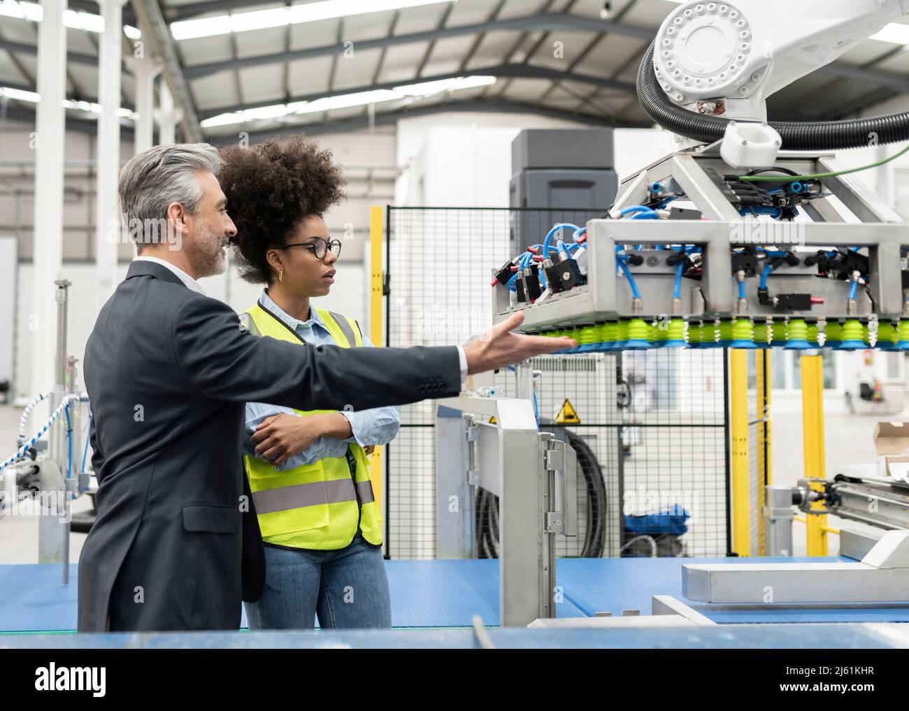 Uomo d'affari che discute con l'ingegnere della macchina robotica a braccio in fabbrica Foto Stock