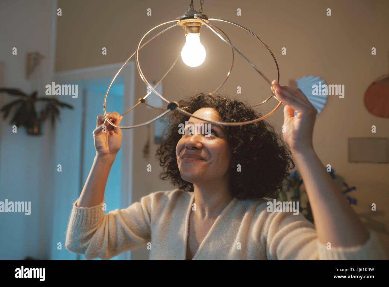 Donna felice con lampada a sospensione illuminata a casa Foto Stock