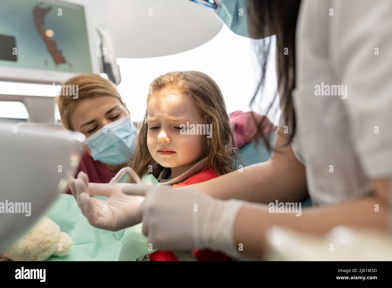 Dentista che parla con la ragazza piccola carina seduta dalla madre alla clinica medica Foto Stock