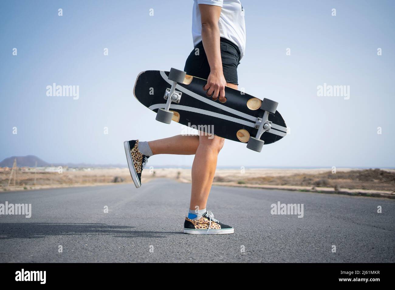 Donna con skateboard in piedi su una gamba su strada Foto Stock